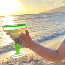 Load image into Gallery viewer, A hand holding a Aunty Lei&#39;s MauiRita in a cactus margarita glass in the beach at sunset.
